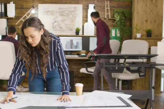 Beautiful caucasian designer working on blueprints in modern cozy office