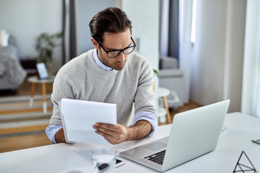 young-businessman-going-through-paperwork-using-laptop-while-working-home